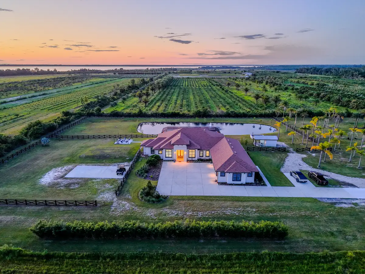 Aerial twilight view of the estate with a pond, drive, and grove